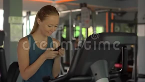 健身房里的一个年轻女子骑着一辆运动自行车手里拿着手机眼前一亮所有的注意都是视频的预览图