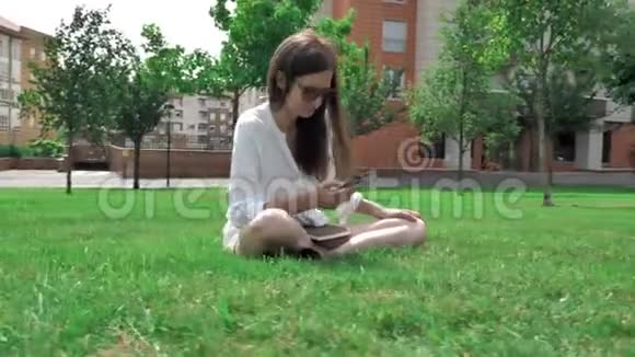 穿着白色衬衫黄色短裤和太阳镜的棕色头发女孩坐在草地上视频的预览图