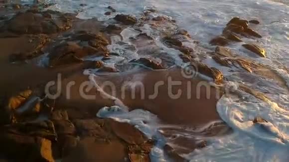 日落时空中飞过海滩上的岩石视频的预览图