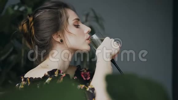 侧视美丽的年轻女子在绿花的背景下在浴室里喝香槟美丽的女士视频的预览图