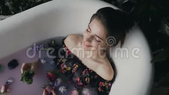 一位年轻女子的肖像她在一个沐浴中微笑放松沐浴中充满了温暖的牛奶水疗中心有许多花蕾视频的预览图