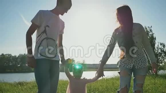 幸福的年轻家庭和女儿在湖边的草地上父母双手抱着女儿把女儿高高举起视频的预览图