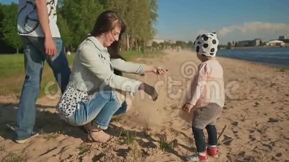 年轻的父母带着女儿在城市水库的岸边玩沙子视频的预览图