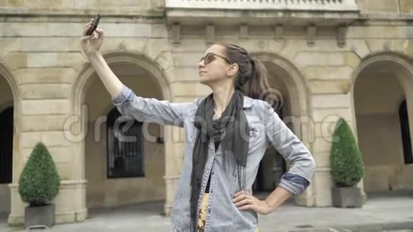 4K漂亮的年轻女孩穿着牛仔裤夹克穿着黄色宽裙在欧洲老街打手机视频的预览图