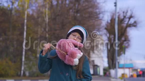 戴眼镜的少女的肖像穿着一件深绿色外套戴着一顶针织帽子带着背包的粉红色袋子视频的预览图