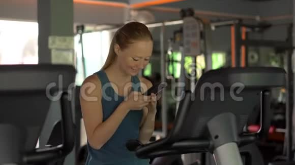 健身房里的一个年轻女子骑着一辆运动自行车手里拿着手机眼前一亮所有的注意都是视频的预览图