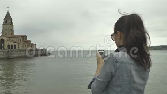4K漂亮的年轻女孩穿着牛仔裤夹克用手机拍摄城市的历史部分视频的预览图