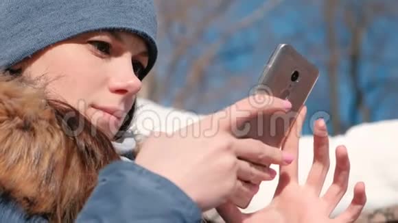 女人坐在冬季公园的手机上浏览网页特写脸视频的预览图