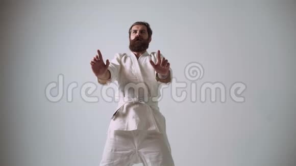 笨拙的空手道挥舞着双手在腹股沟里打自己穿着白色和服的有趣的空手道战士视频的预览图