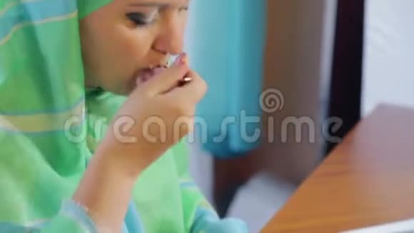 一个身穿浅色围巾的年轻穆斯林妇女在咖啡馆里吃蛋糕喝茶视频的预览图