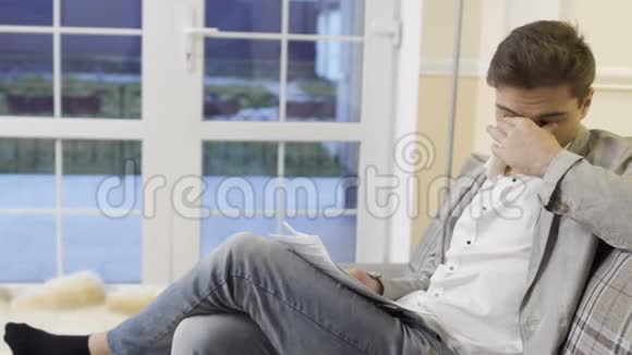 一个疲惫的年轻人坐在家里的沙发上视频的预览图