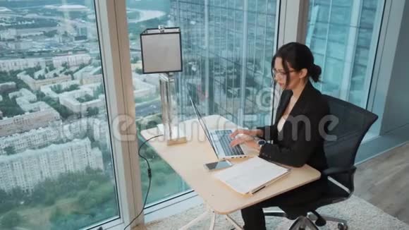 年轻的商务女性在一个位于摩天大楼高层的现代办公室里用笔记本电脑工作视频的预览图