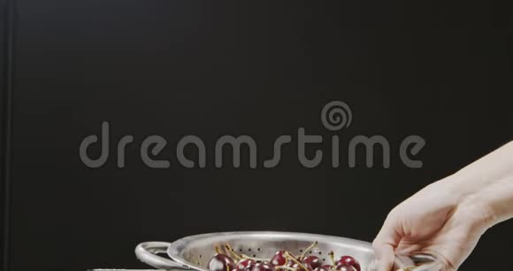 一个女人她的手举起一个带有成熟的湿樱桃的香菜从它流出水溅起水花滴在黑色上视频的预览图