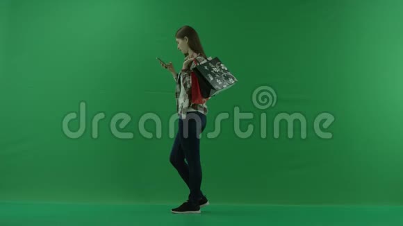 女孩站在她的左边肩膀上放着袋子在绿色的屏幕上在手机里写一些东西视频的预览图