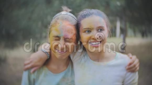 两个十几岁的女孩涂抹了彩色粉末霍利在夏季公园里慢动作地洒水视频的预览图