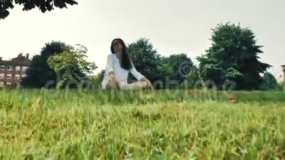 穿着白色衬衫黄色短裤和太阳镜的棕色头发女孩坐在草地上视频的预览图