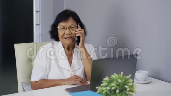 高级妇女在用手机和笔记本电脑说话视频的预览图