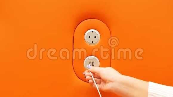 女孩将智能手机插入橙色墙上的USB充电端口视频的预览图