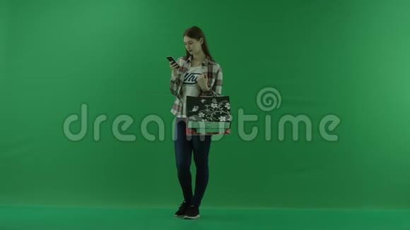 带着袋子的女孩站在半个转弯处看着左边在绿色屏幕上的手机里写了一些东西视频的预览图