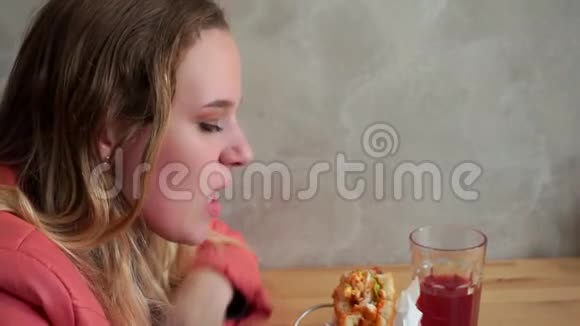 一个年轻饥饿的女孩在吃汉堡包坐在咖啡馆的桌子旁视频的预览图