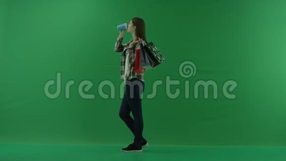 女孩站在她的左边肩膀上放着袋子在绿色的屏幕上喝着杯子里的东西视频的预览图