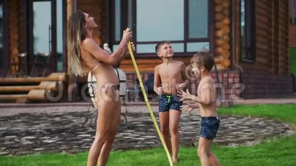 妈妈带着两个孩子玩花园水管把水浇在草地上视频的预览图
