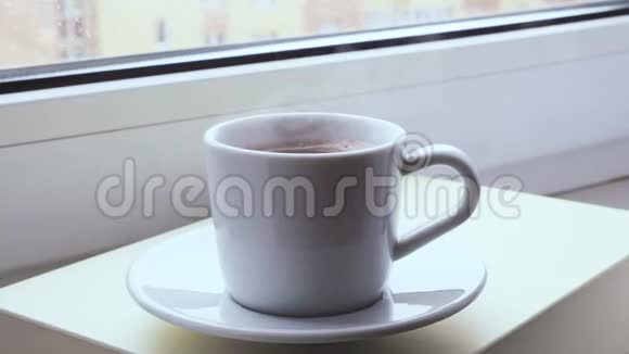 在白雪皑皑的冬日早晨热气腾腾的咖啡杯站在窗户上背景下的雪女人的手拿起一个杯子视频的预览图