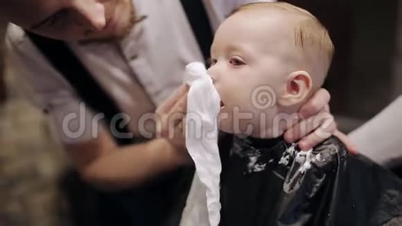 一个男理发师在一家理发店里刮一个小男孩的胡子视频的预览图