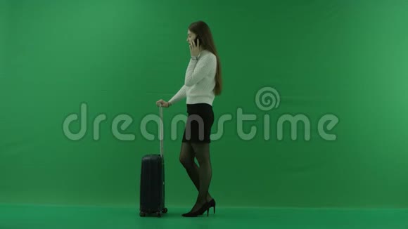 女孩站在她的左边在手提箱旁边在绿色屏幕上打电话视频的预览图
