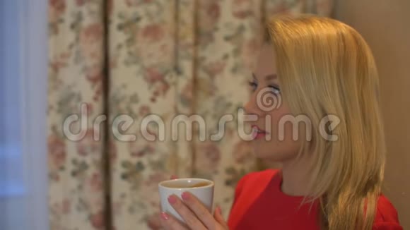 美丽的金发女人手拿杯子热咖啡靠近视频的预览图