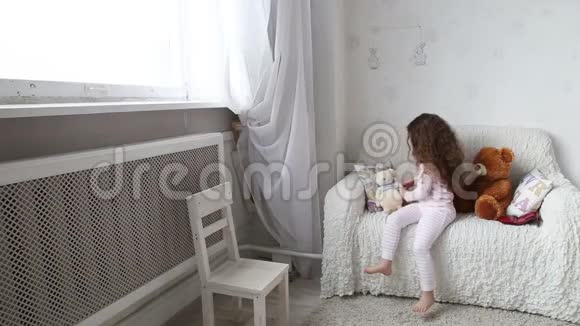 小女孩在沙发上玩玩具熊看着窗外视频的预览图