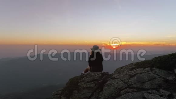 年轻女子坐在山顶或日落的山峰上视频的预览图