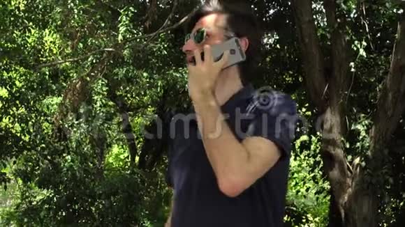 在森林或公园里通过智能手机进行迷人的情感成熟男人交谈视频的预览图