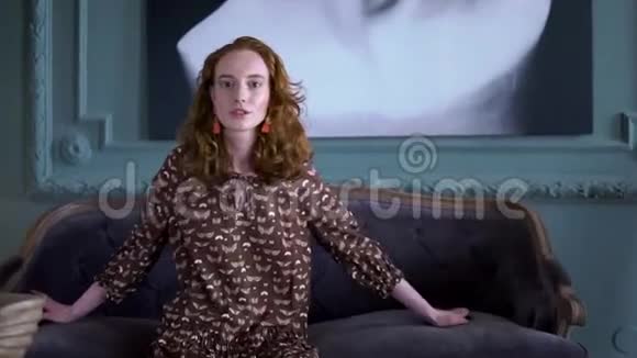 快乐积极的女孩坐在沙发上对着镜头摆姿势视频的预览图