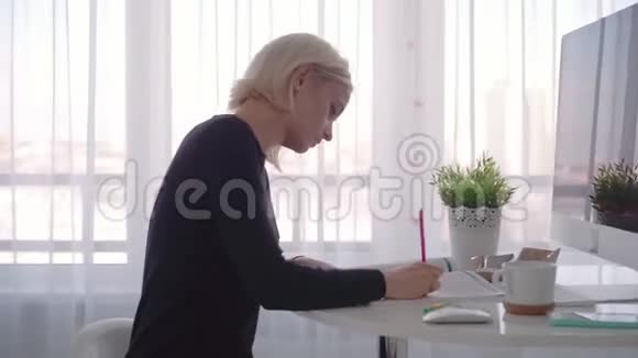 侧视年轻的商务女性坐在桌子旁在笔记本上做笔记博客视频的预览图