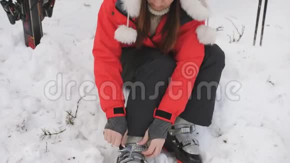 准备滑雪的年轻女子她穿上鞋子坐在滑雪场的雪地里视频的预览图