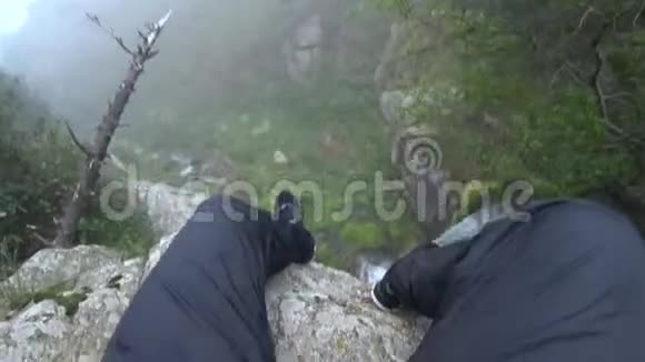 坐在悬崖上腿挂在瀑布上史诗般的画面瀑布的边缘视频的预览图