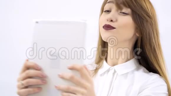 美丽的女孩在白色背景的平板电脑上自拍视频的预览图