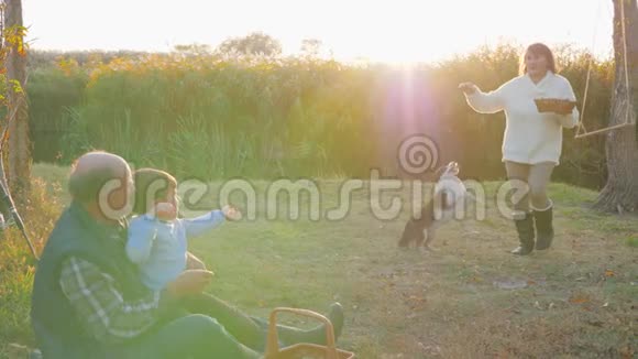 祖父带着孙子坐在背景夕阳下的格子布上在野餐时等待祖母送来的甜馅饼视频的预览图