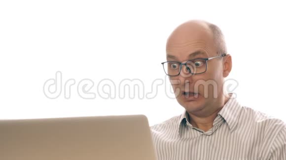 一个戴眼镜的商人的肖像带着惊恐的神情坐在办公室的笔记本电脑前害怕地把自己擦进去视频的预览图