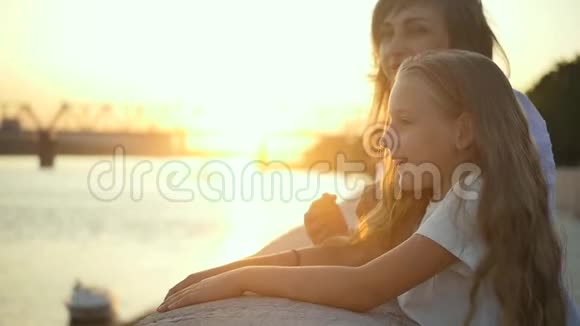 妈妈在女儿旁边欣赏城市日落在夕阳西下的背景下爱妈妈和女儿视频的预览图