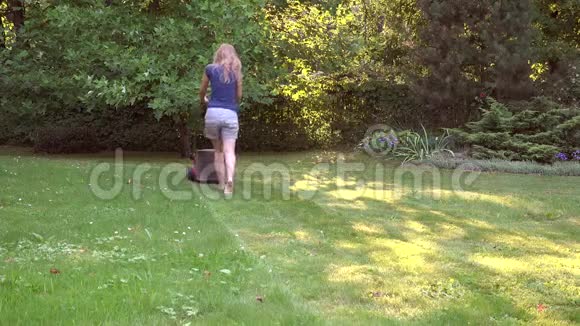 赤脚女人用割草机在绿色花园里割草4K视频的预览图