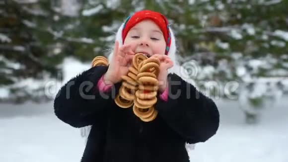 穿着毛皮外套和俄罗斯风格的红领巾的小女孩吃雪和森林背景下的百吉饼视频的预览图