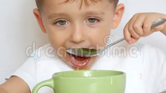 孩子用汤匙从盘子里紧紧地吃汤男孩把勺子放进嘴里视频的预览图