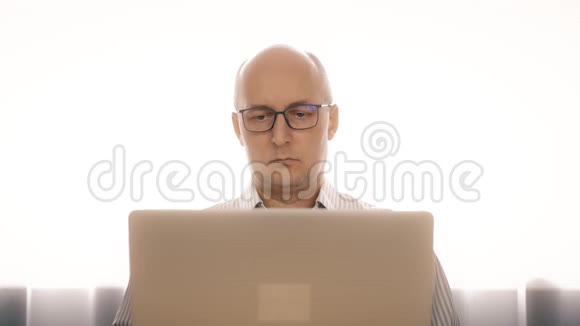 戴眼镜的悲伤男人在笔记本上工作因为疲劳而揉眼睛视频的预览图