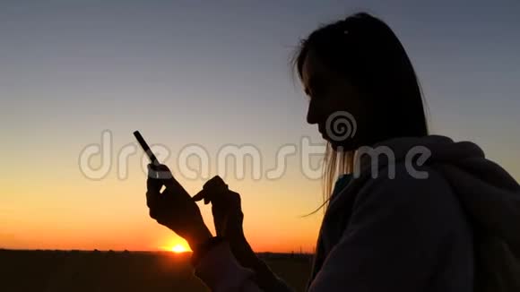 日落时分使用智能手机的女性剪影视频的预览图