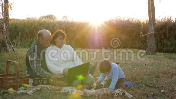 老人和妻子在日出的背景下与孙子一起用笔记本电脑野餐视频的预览图