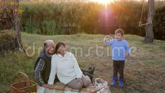孩子在日落时分和祖母和祖父一起在小河边休息时喂狗视频的预览图