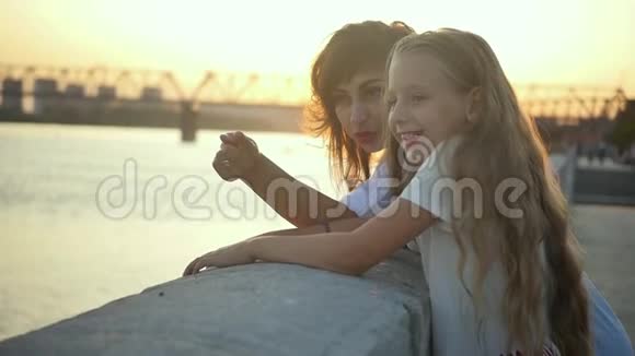 妈妈在女儿旁边欣赏城市日落在夕阳西下的背景下爱妈妈和女儿视频的预览图