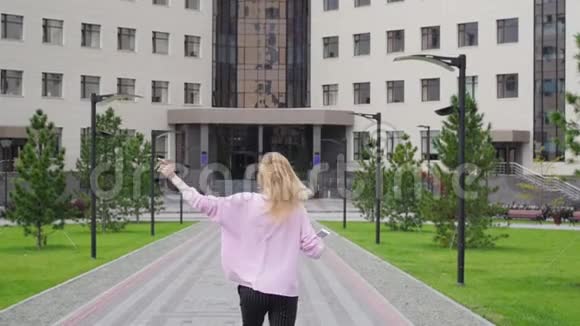 大学背景下的年轻女子手里拿着手机跳着舞穿粉色衣服的女学生视频的预览图